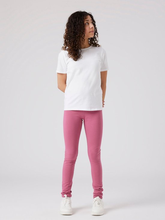 Meisje met krullend haar, een witte T-shirt en roze legging, staand.