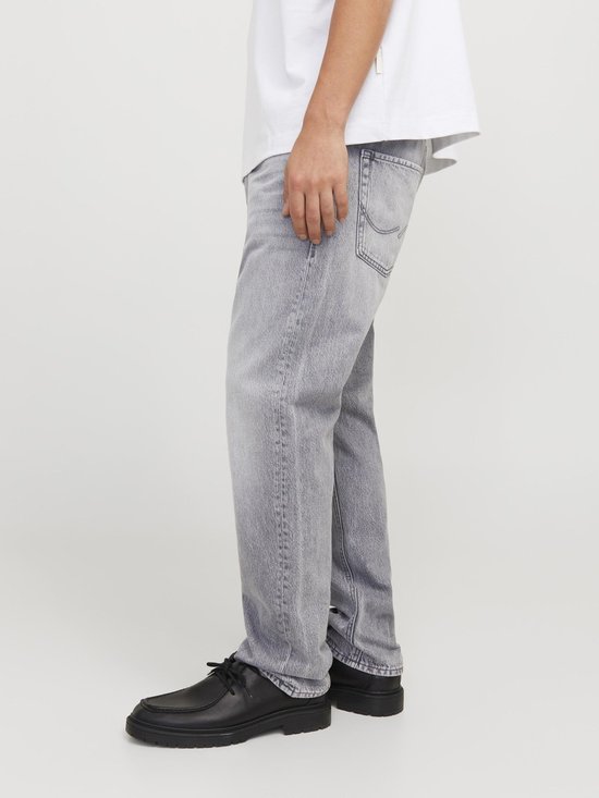 Zij-aanzicht van een man in witte T-shirt en grijze jeans.