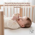 Baby in bedje bijt op de pastelkleurige rammelaar en bijtring.