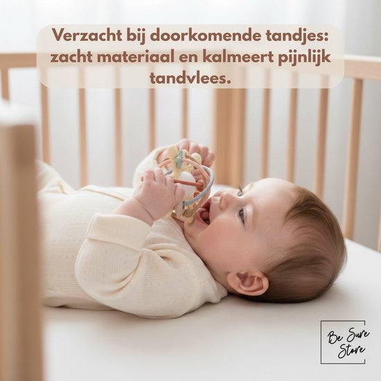 Baby in bedje bijt op de pastelkleurige rammelaar en bijtring.