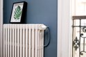 Netatmo slimme thermostaatknop, wit met oranje accent, op een crèmekleurige gietijzeren radiator.
