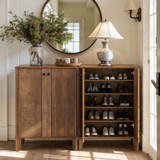 Houten schoenenkast met open deuren, gevuld met schoenen. Een spiegel, lamp en plant staan bovenop.