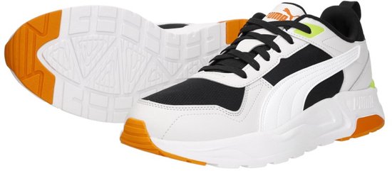 Wit leren sneaker met zwarte mesh, witte Puma-streep en oranje zolen. Een tweede sneaker ligt ernaast.