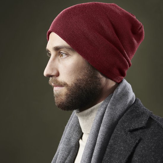Man met baard draagt een wijnrode muts, grijze sjaal en coltrui.