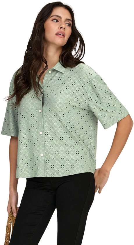 Model met lichtgroene blouse met broderie anglaise en zwarte broek.