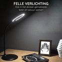 Lampe de bureau noire avec éclairage LED rond, posée sur un bureau à côté d'un livre et d'un cadre photo.
