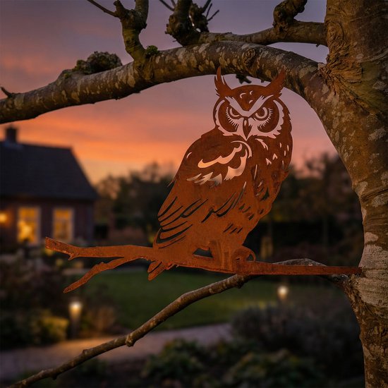 Roestbruine metalen uil van cortenstaal, zittend op een tak bij zonsondergang.