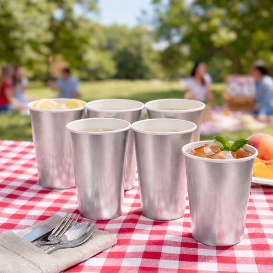 Zilverkleurige feestbekers op een rood-wit geruite picknickdeken, met dranken en citroen.