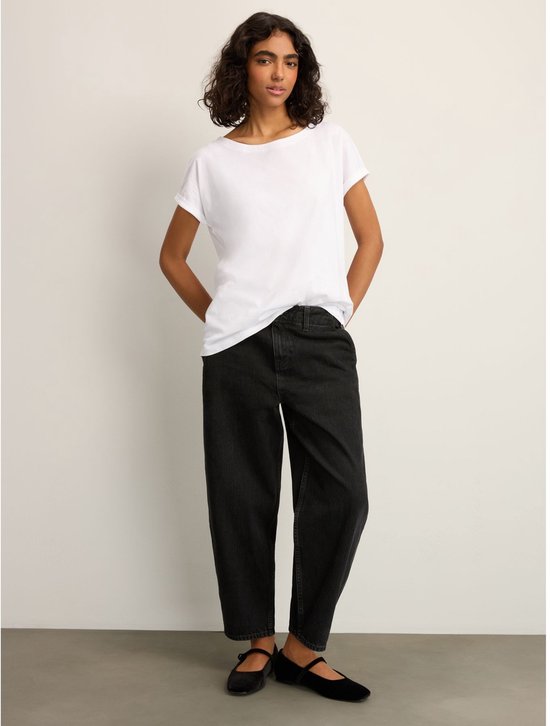 Een vrouw met krullend donker haar draagt een wit T-shirt met opgerolde korte mouwen en een ronde hals, en zwarte broek.