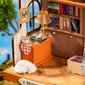 Miniatuur boekenwinkel interieur met boeken, lamp, kopje thee en slapende kat op een oranje kast.