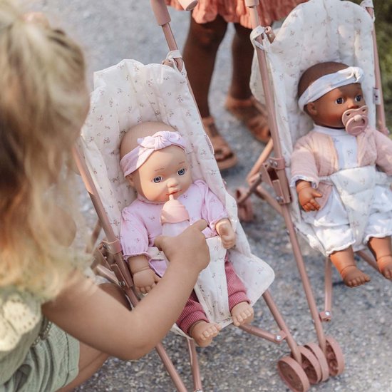 Een meisje geeft een pop in een roze kinderwagen met bloemenprint een flesje te drinken.