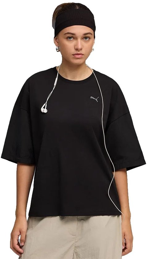 Model draagt een zwarte PUMA oversized T-shirt met korte, wijde mouwen, een grijze PUMA-logo op de borst, met koptelefoon en hoofdband.