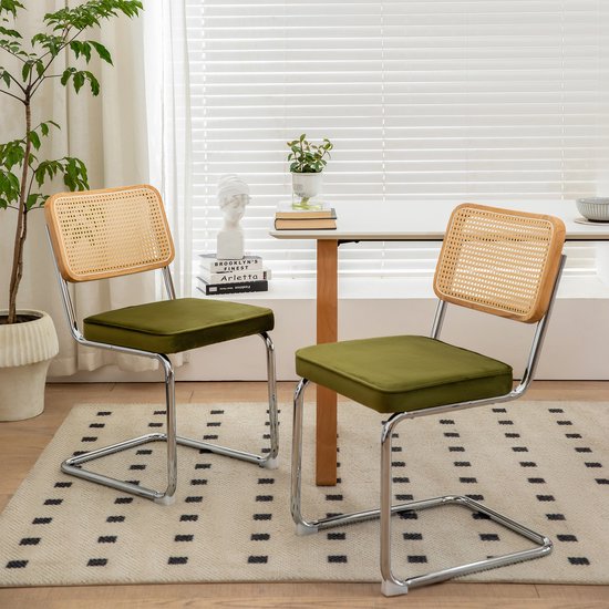 Twee groene stoelen met rieten rugleuningen en chromen sledepoten, in een woonkamer bij een tafel.