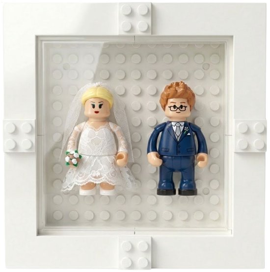 Minifiguur bruid in witte jurk en bruidegom in blauw pak in een witte fotolijst met bouwsteen-achtergrond.