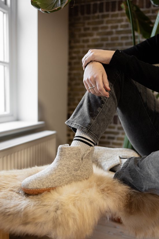 Zittend persoon in grijze jeans met een lichtgrijze vilten pantoffel op een wollen kleed.