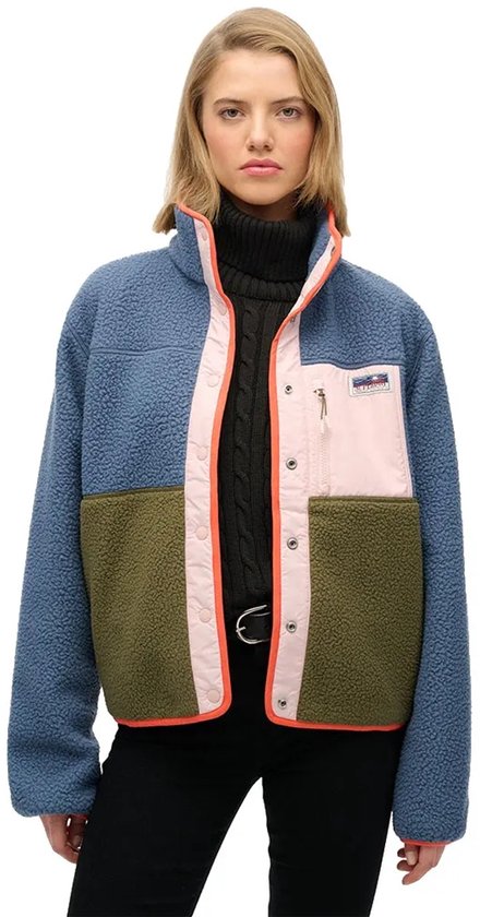 Model draagt een blauwe fleece jas met opgestikte panelen in roze en kaki. Oranje bies.