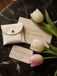 Crèmekleurig Lundholm etui, kaartje met 'Elegance in simplicity' en merkkaartje tussen witte en roze tulpen.