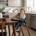 Enfant aux cheveux bouclés dans une chaise haute Deryan noire avec pieds aspect bois, mangeant sur un plateau.