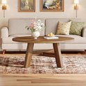 Ronde salontafel met walnootkleurige afwerking, staand op een perzisch tapijt, naast een bank.