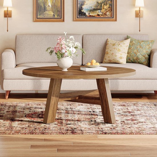 Ronde salontafel met walnootkleurige afwerking, staand op een perzisch tapijt, naast een bank.