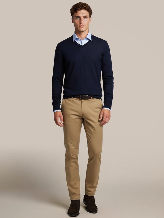 Man met donkerblauwe V-hals trui, lichtblauwe overhemd en lichtbruine chino broek.