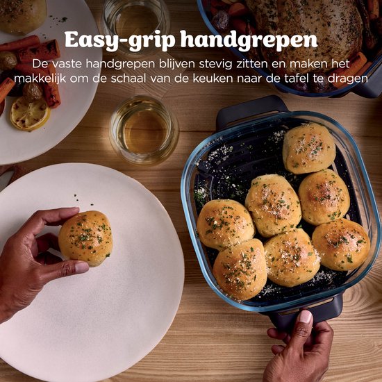 Een hand pakt een kruidenbroodje uit een glazen schaal met meer broodjes en kruiden.
