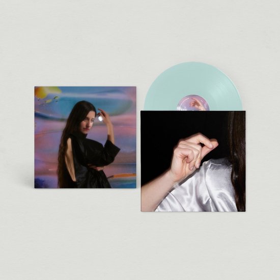 Een lichtblauwe vinylplaat met hoes. De hoes toont een vrouw in een zwarte outfit op een abstracte, kleurrijke achtergrond.