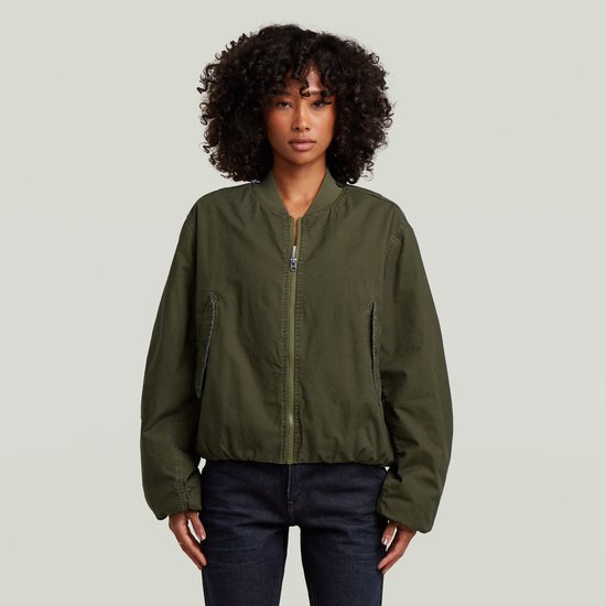 Model met krullend haar draagt een groene bomberjack met ritssluiting en witte top.