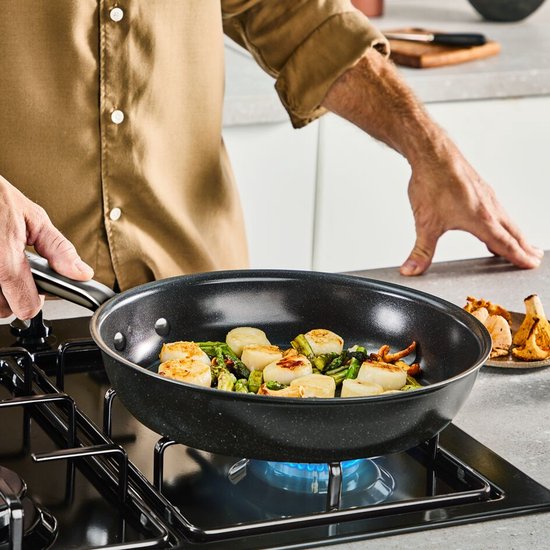 Man kookt sint-jakobsschelpen, asperges en paddestoelen in een Tefal koekenpan op inductie.