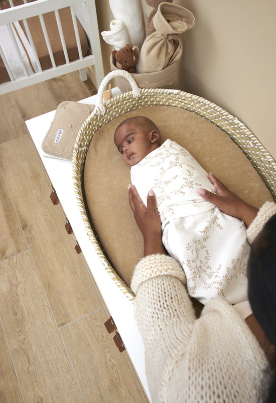 Baby in een wit Meyco inbakerdoek met takjesprint, op een aankleedkussen.