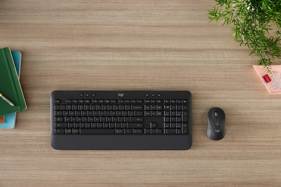 Donkergrijs Logitech toetsenbord en muis op een houten bureau met een plant.