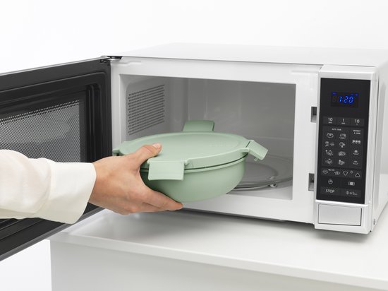 Main plaçant une boîte à salade vert pâle dans un micro-ondes.