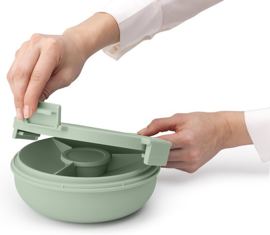 Une main place l'insert de couvercle segmenté dans une boîte à salade verte jade.