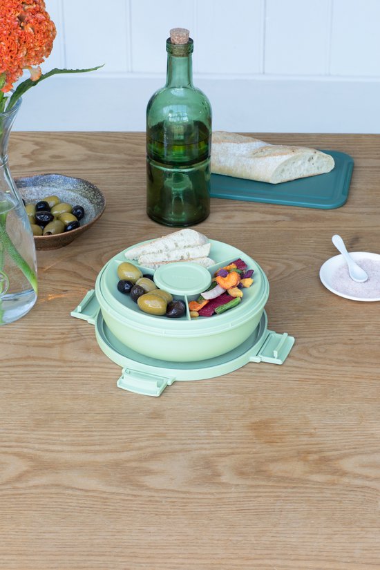 Boîte à salade vert pâle sur une table, remplie de salade, d'olives et de pain.