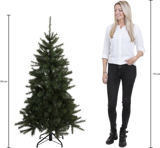 Een 155 cm hoge, volle groene kunstkerstboom naast een 175 cm lange vrouw.