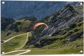 WallClassics - Tuinposter – Paraglidend door de Bergen en Natuur - 75x50 cm Foto op Tuinposter  (wanddecoratie voor buiten en binnen)