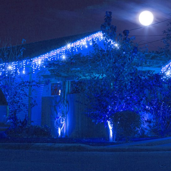 Nachtelijk uitzicht op een huis versierd met blauwe LED-ijspegelverlichting onder een heldere volle maan.