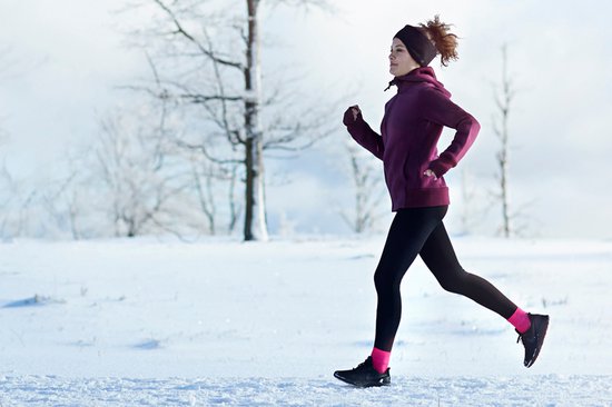Vrouw in paarse hoodie en zwarte legging, joggend in de sneeuw.