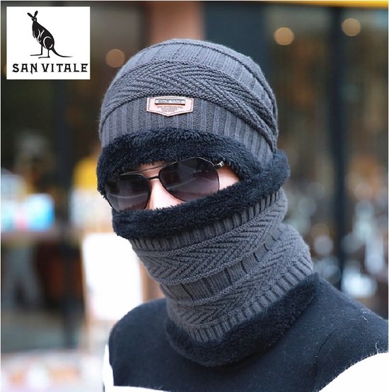 Man met donkergrijze muts en col, met zwarte fleece voering, en zonnebril.