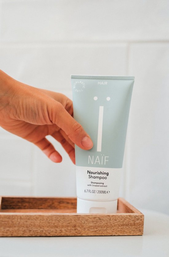 Een hand pakt een turquoise Naïf shampoo tube uit een houten bakje.