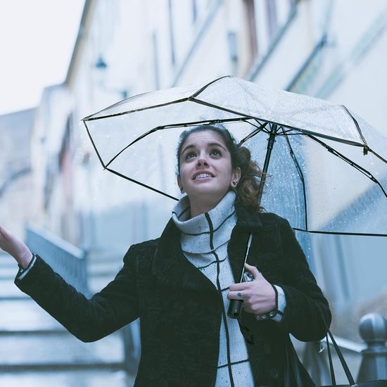 Vrouw met een doorzichtige paraplu in de regen, met de mond open en omhoog kijkend.