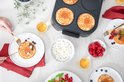 Bovenaanzicht van een Fritel pannenkoekenmaker met 4 pannenkoeken, geserveerd op borden met toppings.