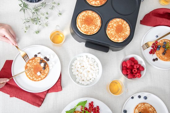 Bovenaanzicht van een Fritel pannenkoekenmaker met 4 pannenkoeken, geserveerd op borden met toppings.