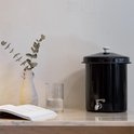 Zwarte waterfilter met chromen kraantje, op een marmeren oppervlak bij een vaas en boek.