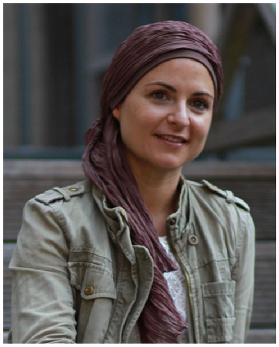 Bruine chemo hoofddoek met plooien, gedragen door een lachende vrouw met beige jas.