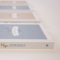 Meerdere 'Mijn Oppasboek' boeken op een rij, in pastelblauw en roze, met kleine driehoekjes en sterretjes.