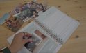 Een open ringband-planner met foto's, een hand die een foto erin schuift.