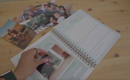 Een open ringband-planner met foto's, een hand die een foto erin schuift.
