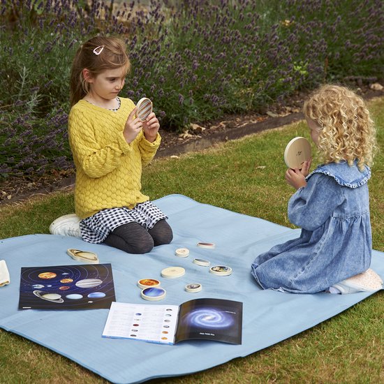Twee kinderen met houten planeten en een boek in de tuin