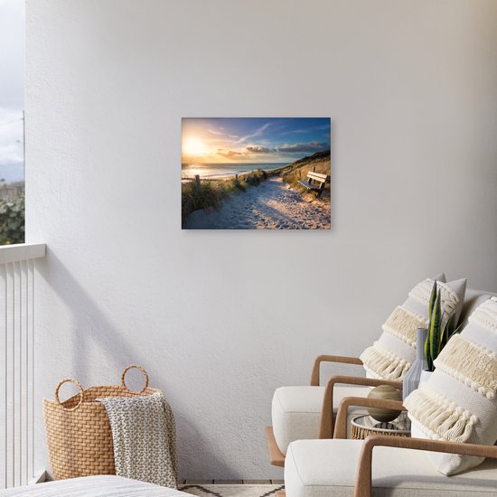 Canvasprint van een strandpad met duinen, gras en een houten bankje bij zonsondergang, aan een witte muur op een balkon.